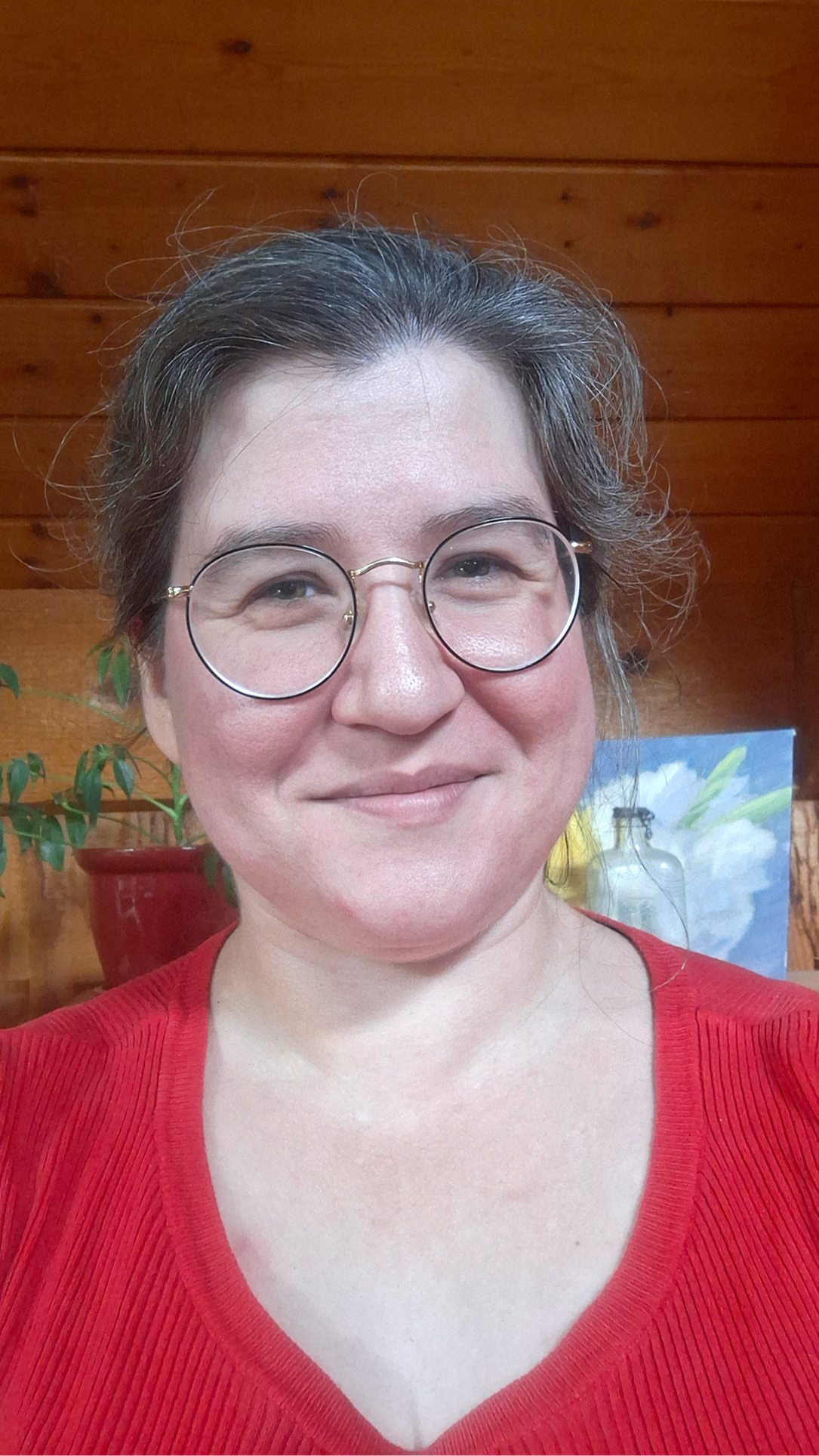 Person wearing glasses and a red shirt with a wooden wall background